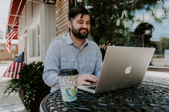 smiling man on laptop with carboard coffee cup sitting on the desk